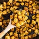 Spoonful of croutons being scooped out of the air fryer basket.