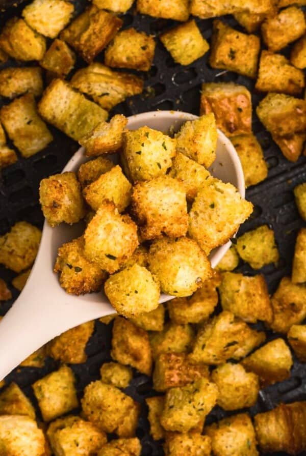 Spoonful of croutons being scooped out of the air fryer basket.