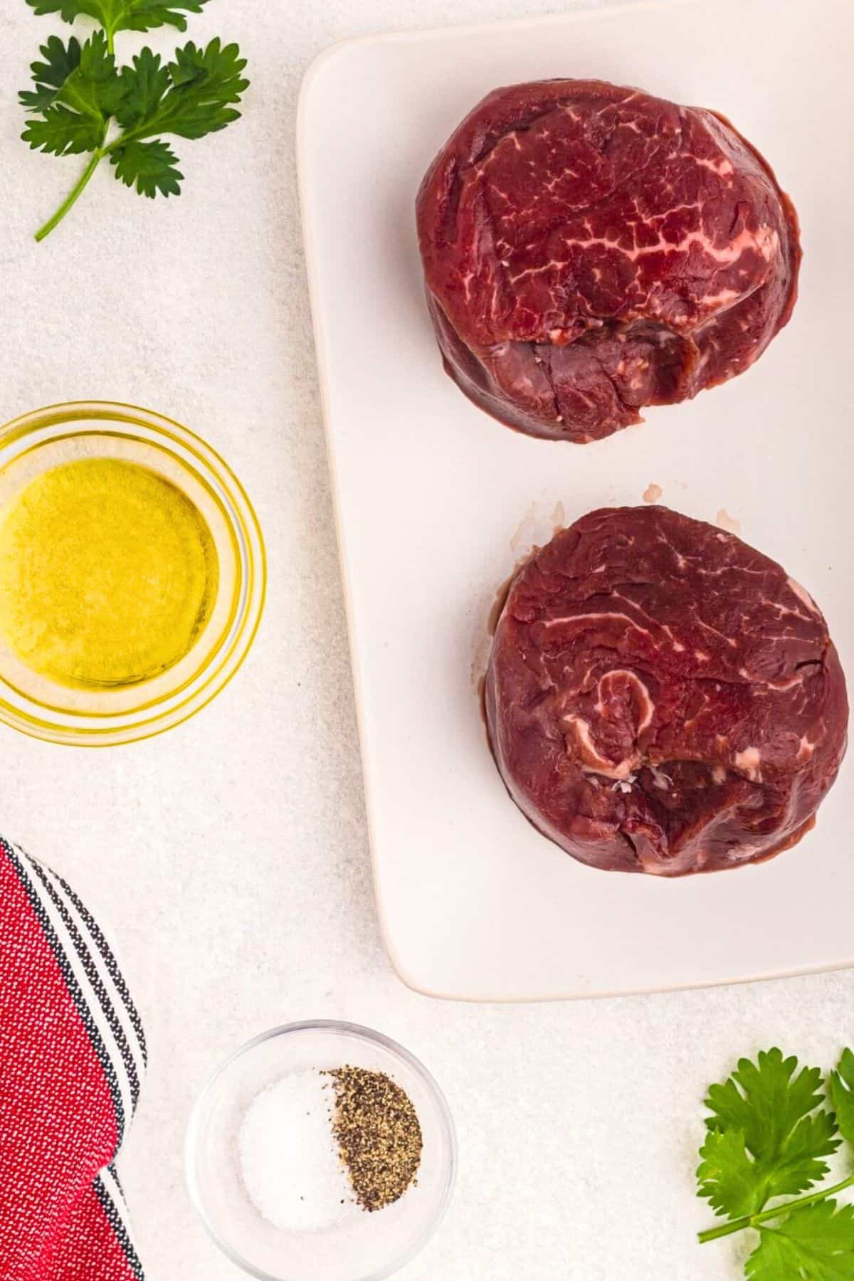 Uncooked filets, olive oil, and salt and pepper on a marble table. 