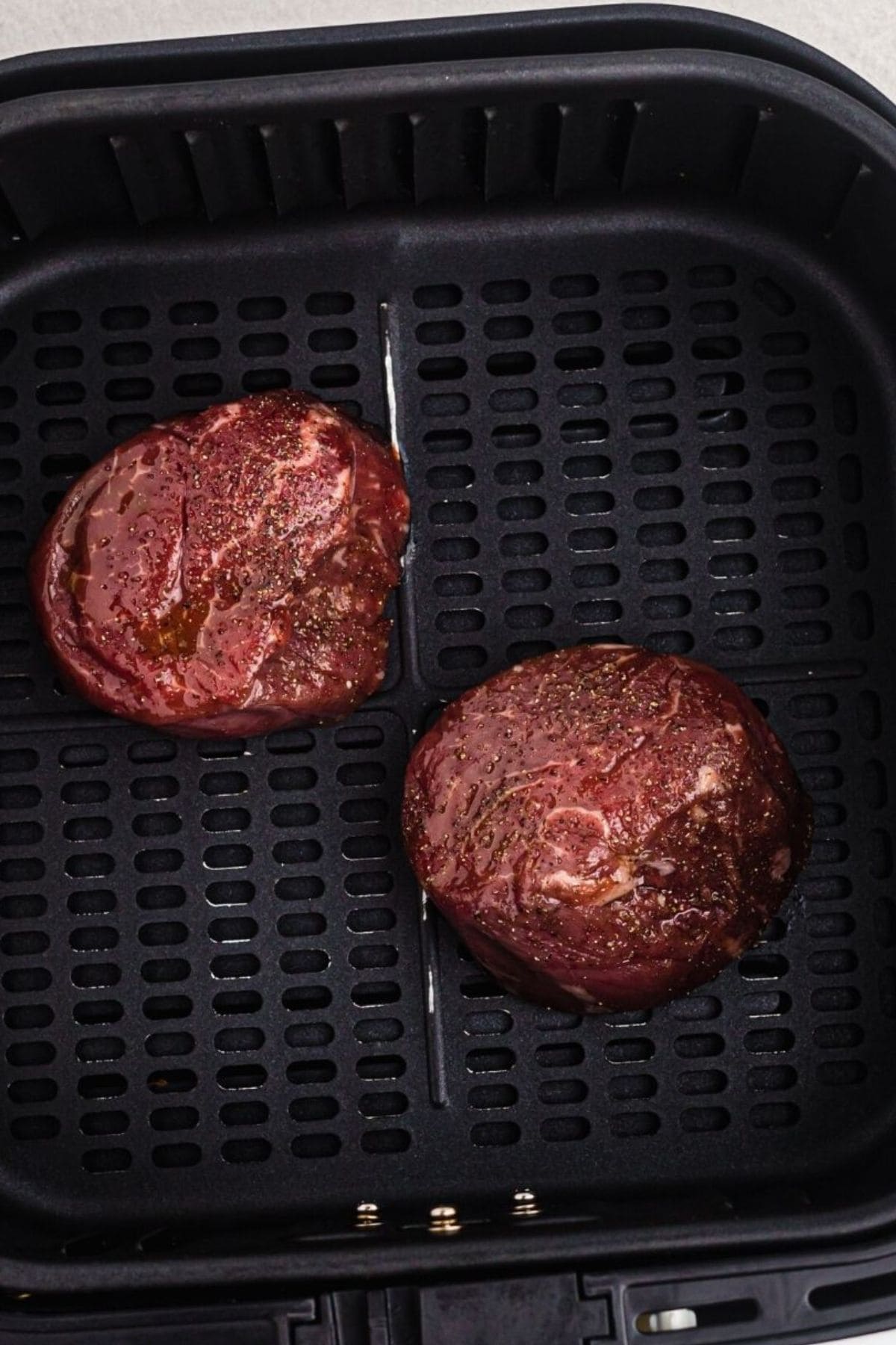 Uncooked filets in the air fryer basket after being seasoned. 