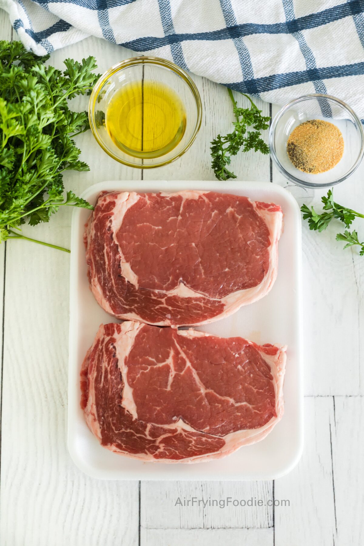 Olive oil, seasonings, and Ribeye steaks on a white table to make steak bites in the air fryer. 