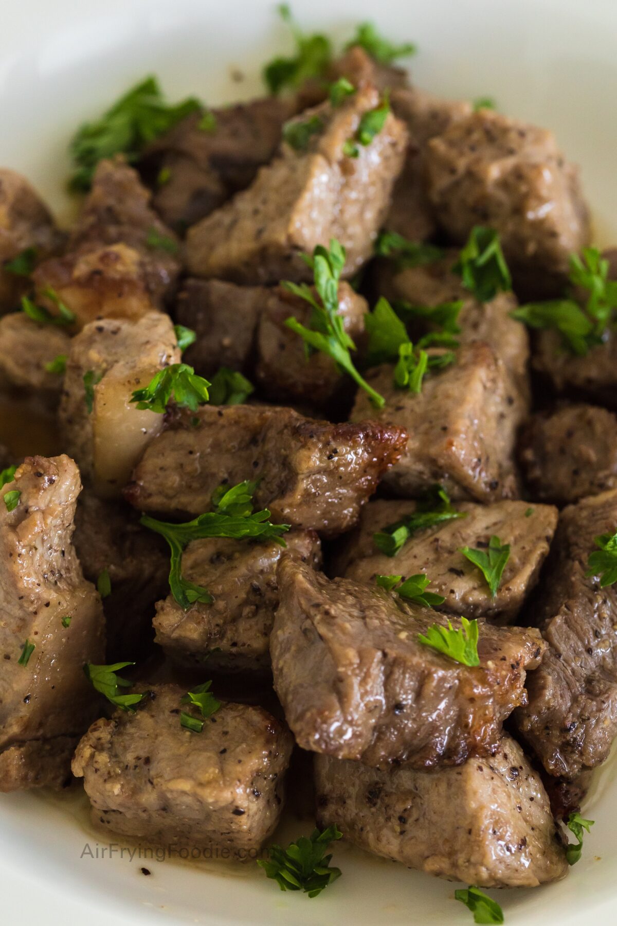 Close up of steak bites made in the air fryer and topped with a garlic butter sauce and fresh chopped parsley.