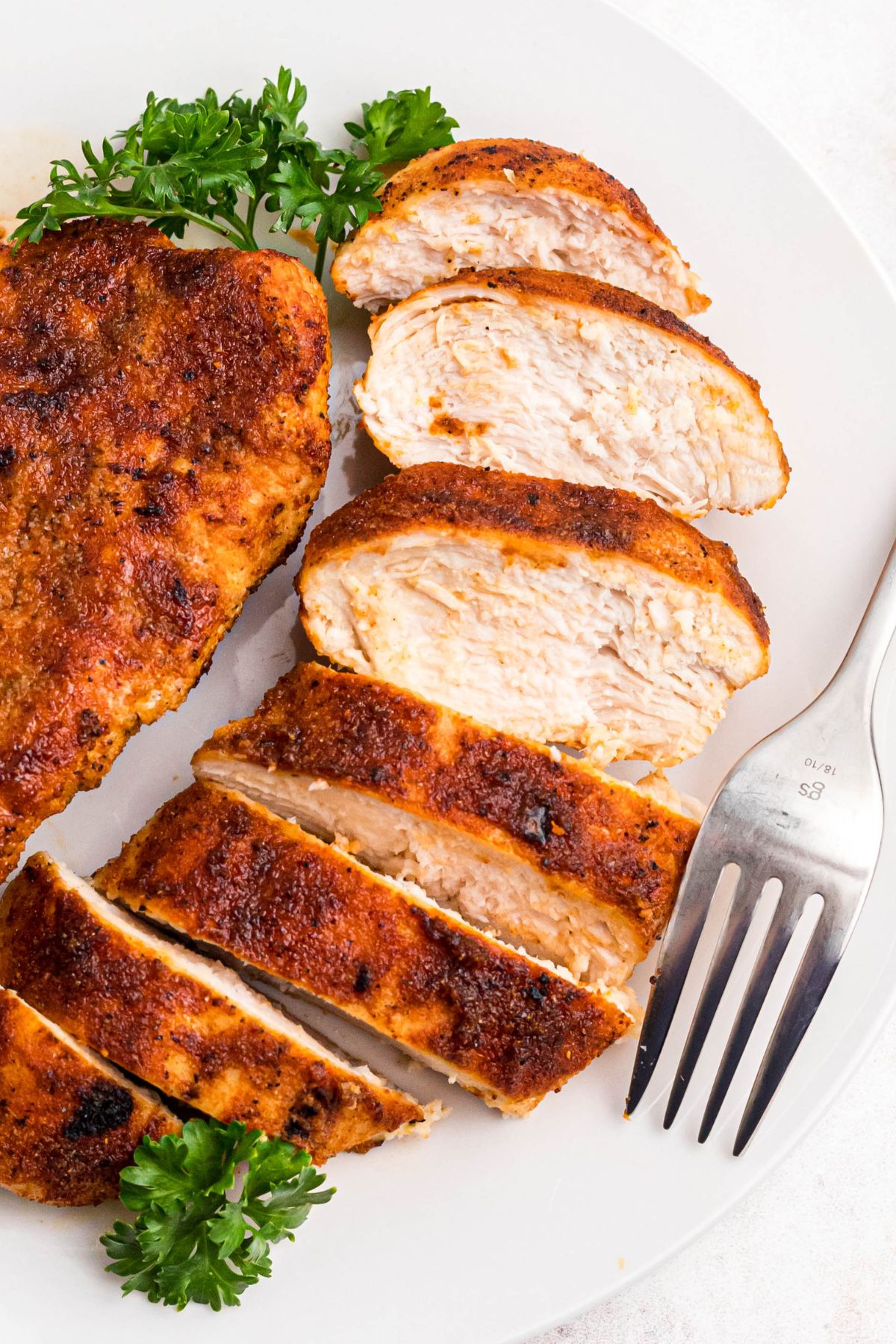 Seasoned chicken breast on a white plate cut into slices. 