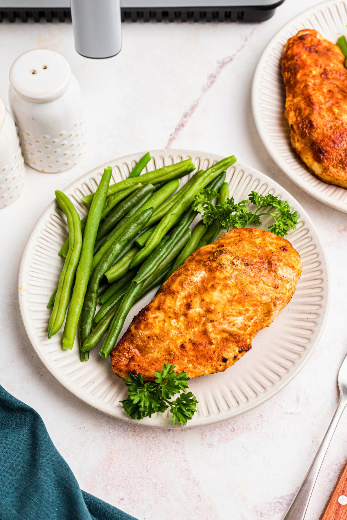 Golden juicy chicken breast on a white plate with green beans on a marble table. 