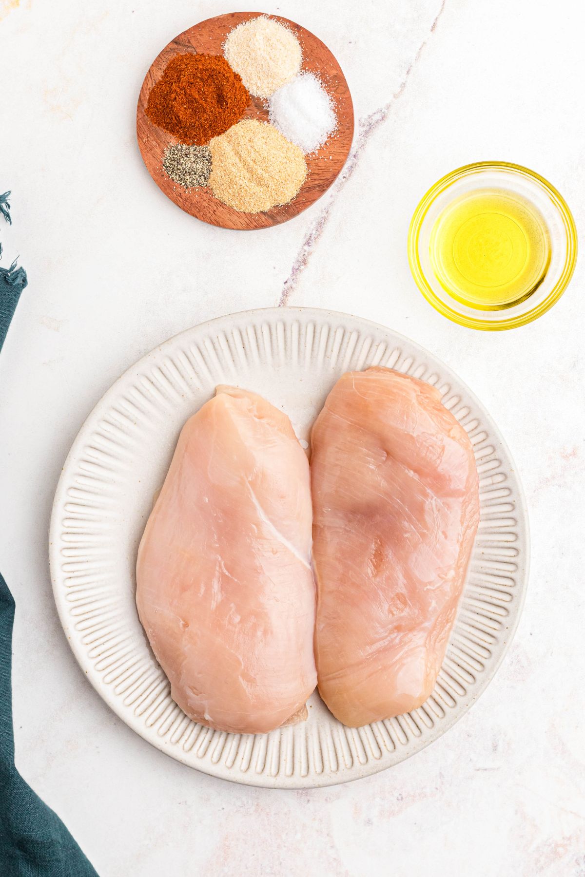 Ingredients needed to make chicken breast in the air fryer measured out on a marble table. 