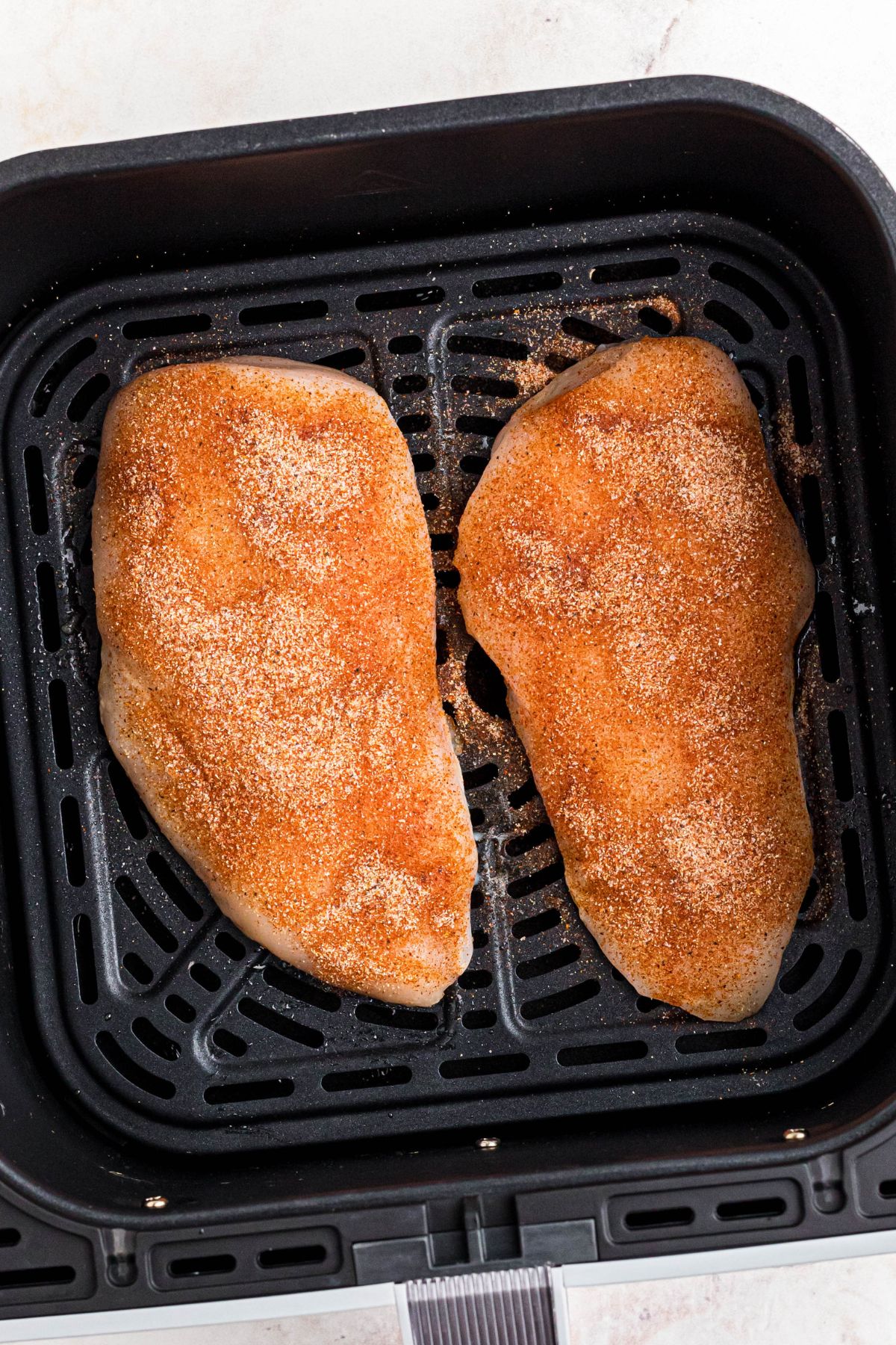 Seasoned uncooked chicken breast in the air fryer basket. 