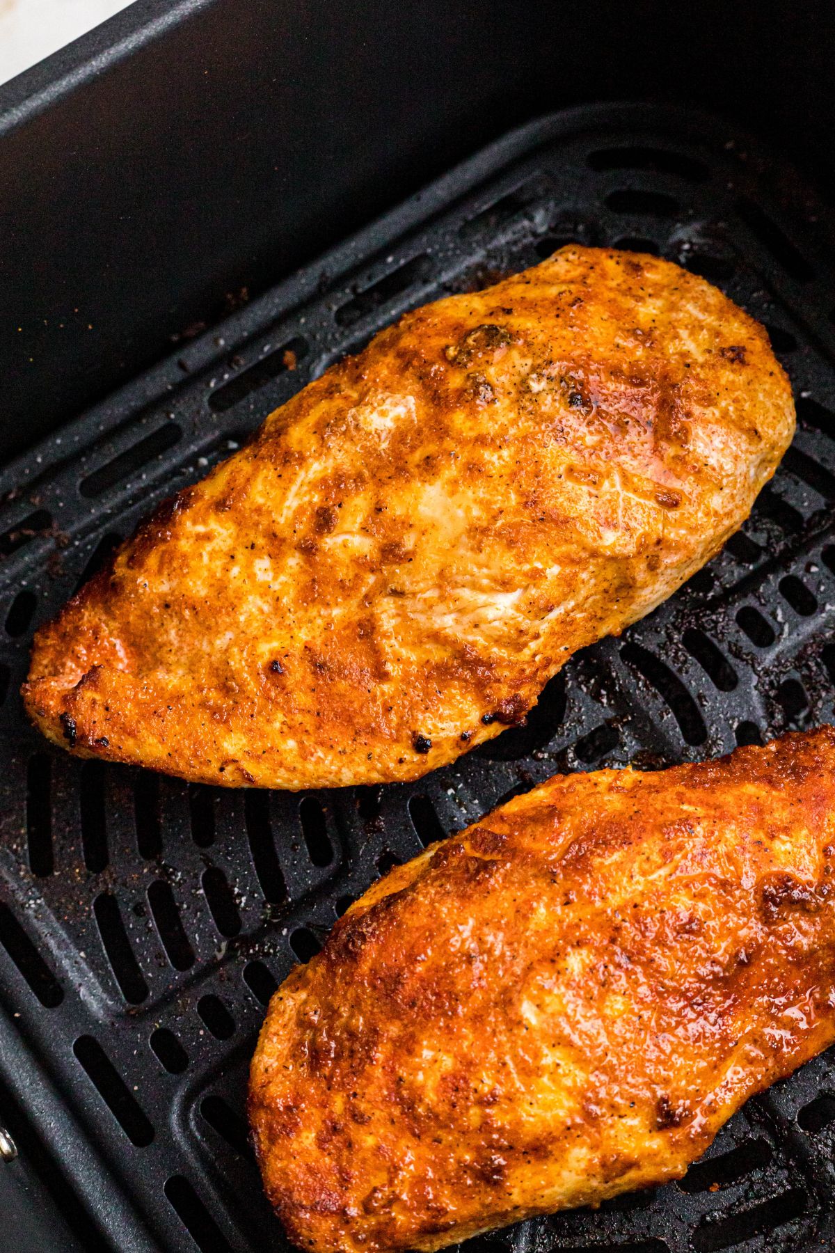 Golden juicy chicken in the air fryer basket after being seasoned and cooked. 