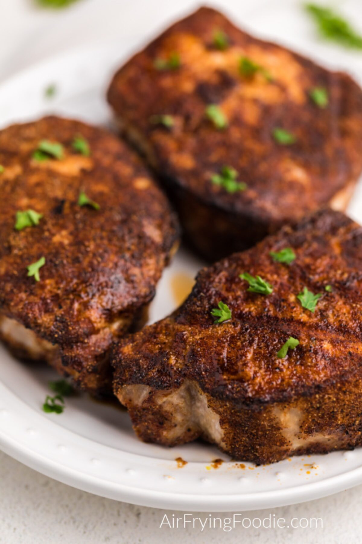 Close up photo of thick cut seasoned and air-fried pork chops on a white plate. 