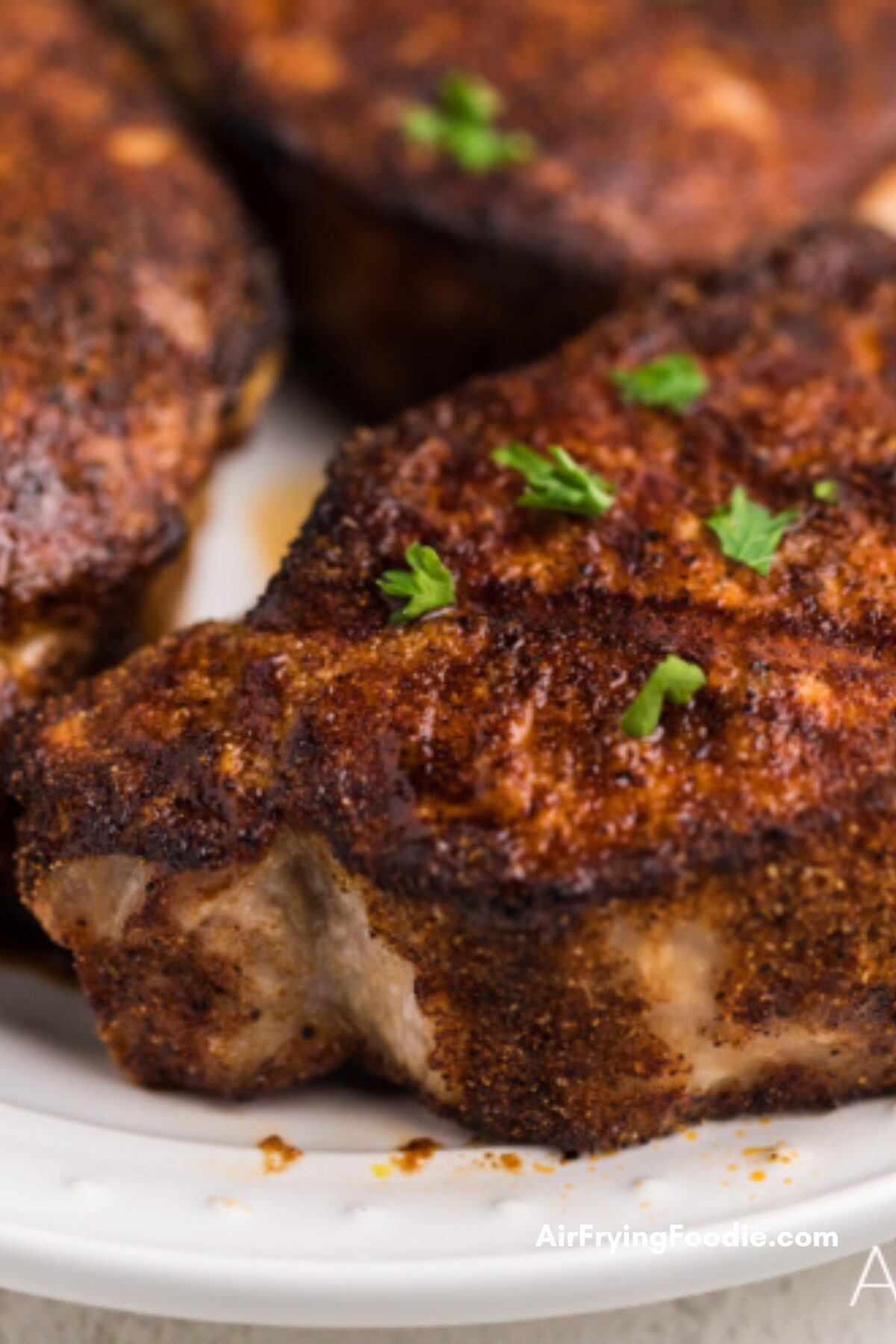 Crispy, seasoned, air fryer pork chops on a white plate, ready to eat. 