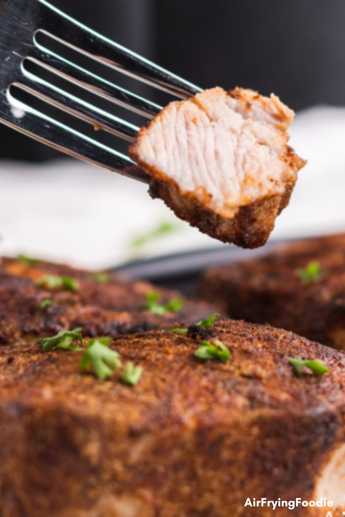 Close up of seasoned air fryer pork chops, with a bite on a fork, ready to eat. 