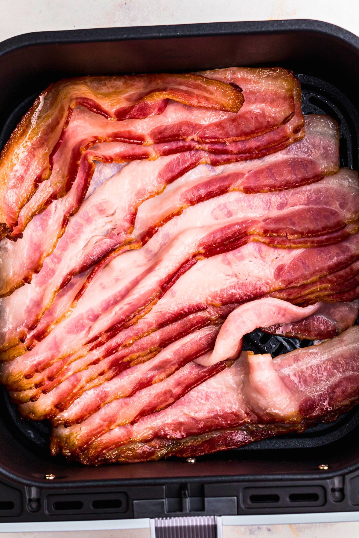 Uncooked thawed bacon in the air fryer basket after being separated  during the air fryer cooking time. 