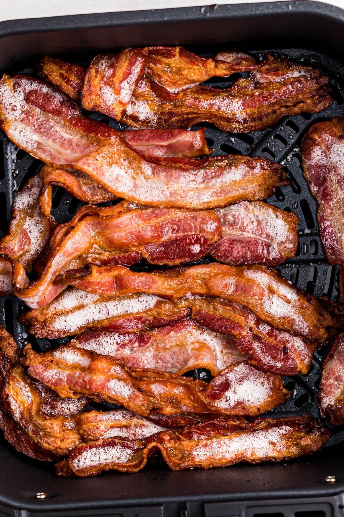 Golden crispy sizzling bacon in the air fryer basket after being cooked. 