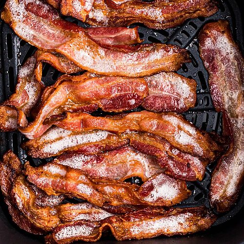 Golden crispy bacon in the air fryer basket after being cooked from frozen.