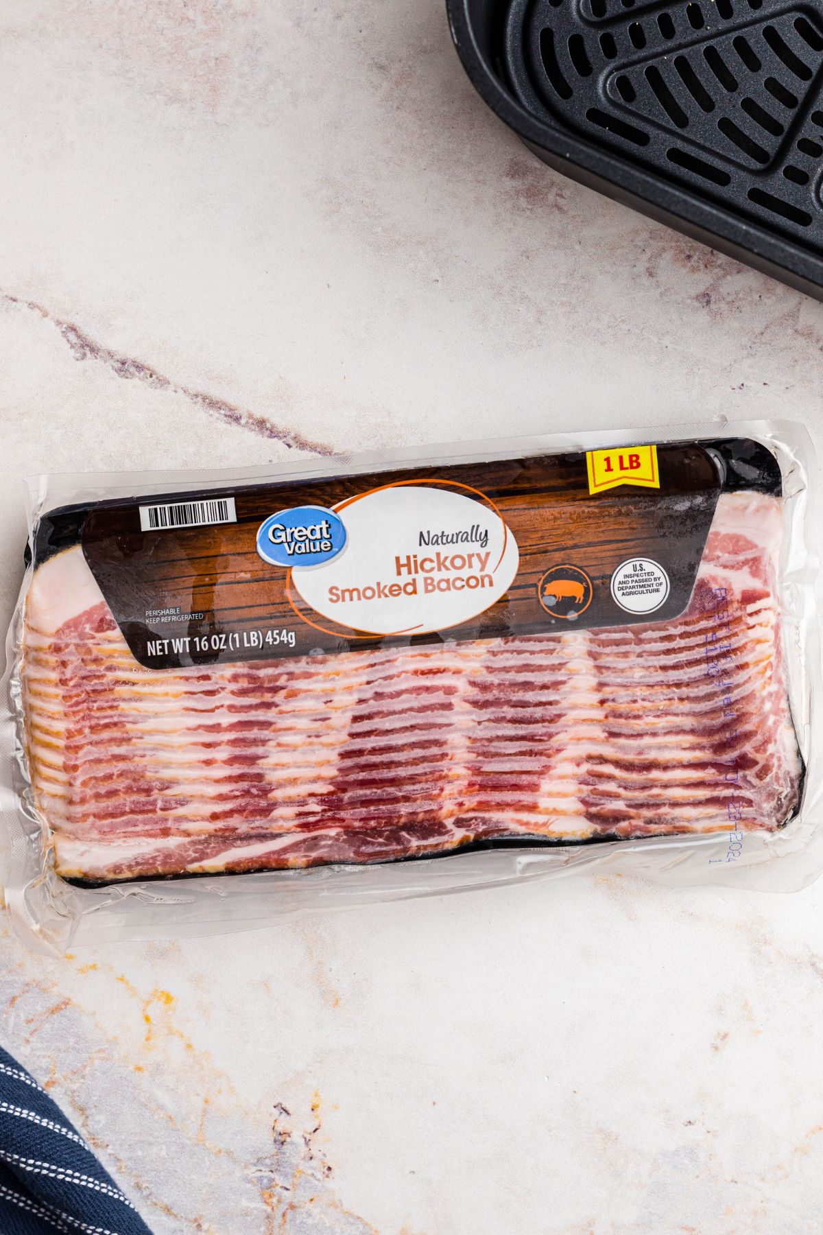 One pound package of frozen bacon in packaging, in front of air fryer basket. 