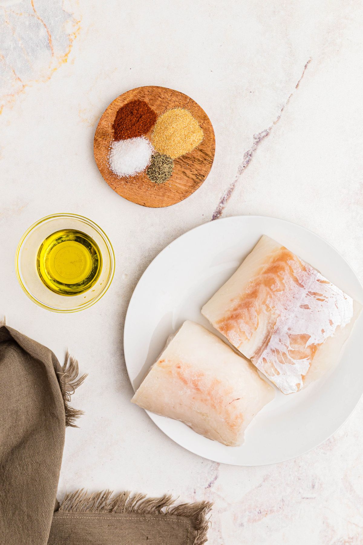 Ingredients measured out on a white marble table along with frozen cod. 