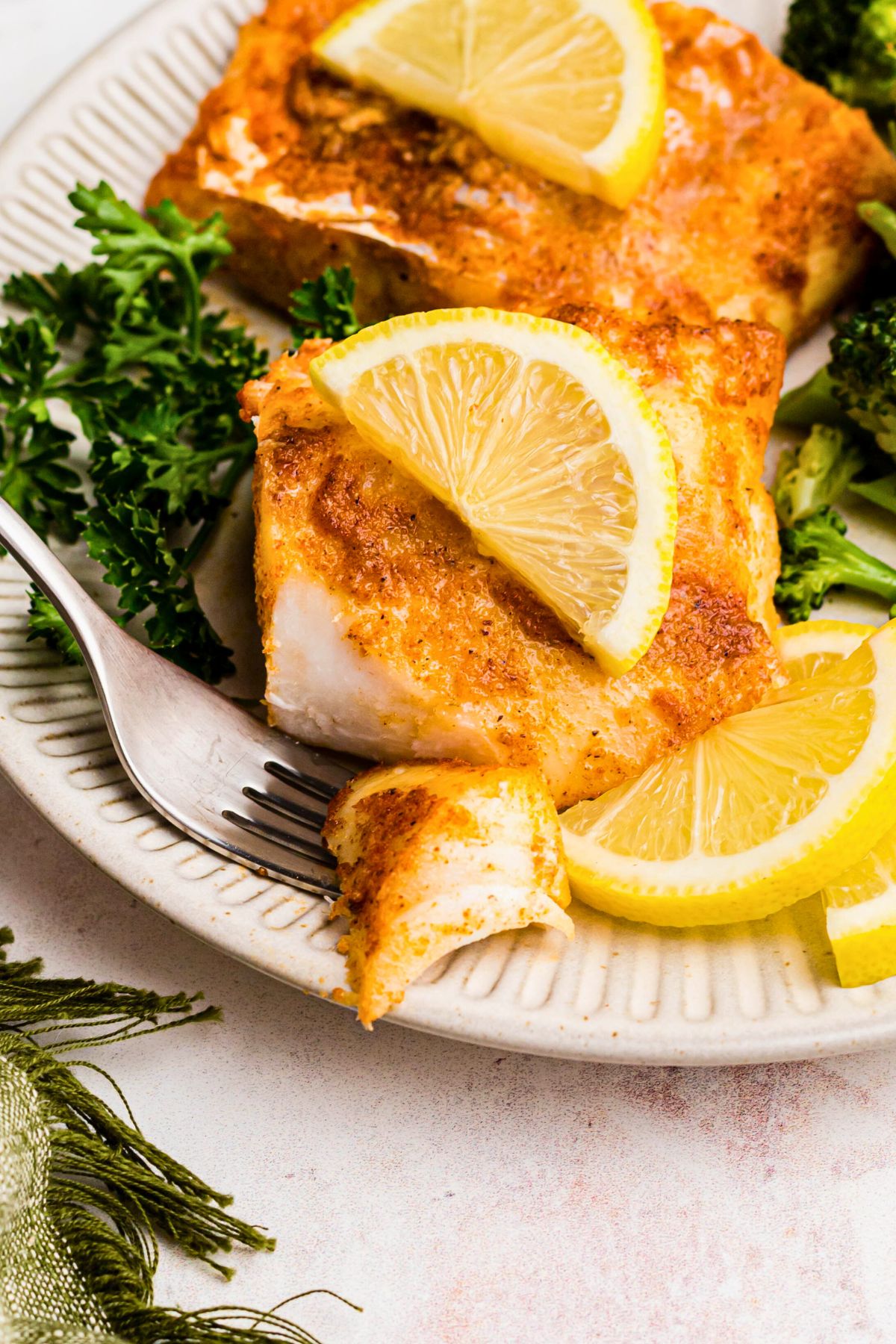 Juicy cod filet on a white plate with a lemon slice and a small piece on a fork. 