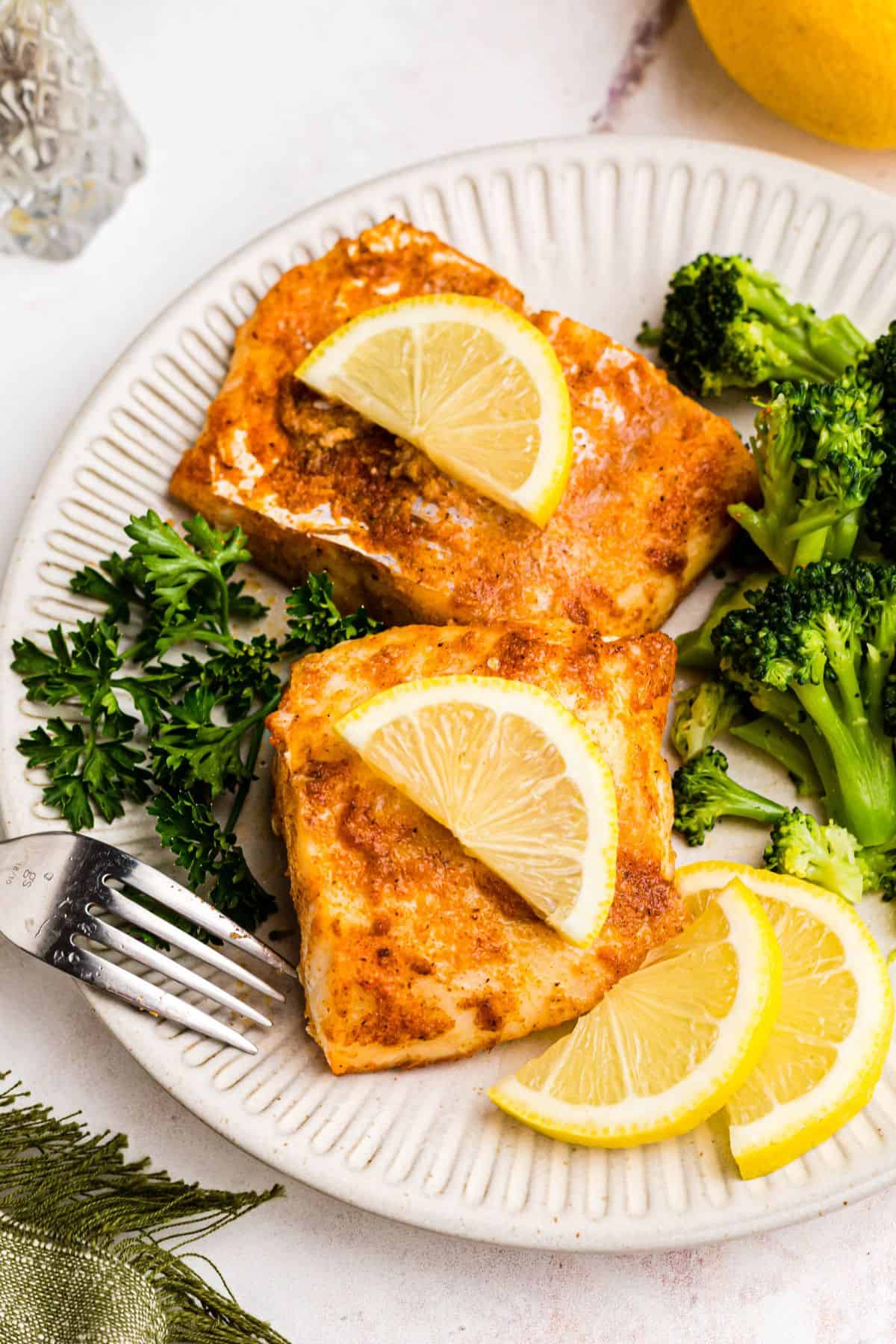 Moist air fried cod on a white plate with broccoli and lemon slices. 