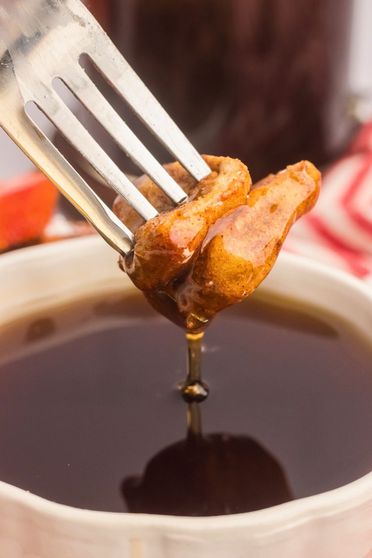 Golden French toast bites on a fork being dipped into syrup.