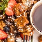 Golden French toast bites on a white plate with berries and syrup.