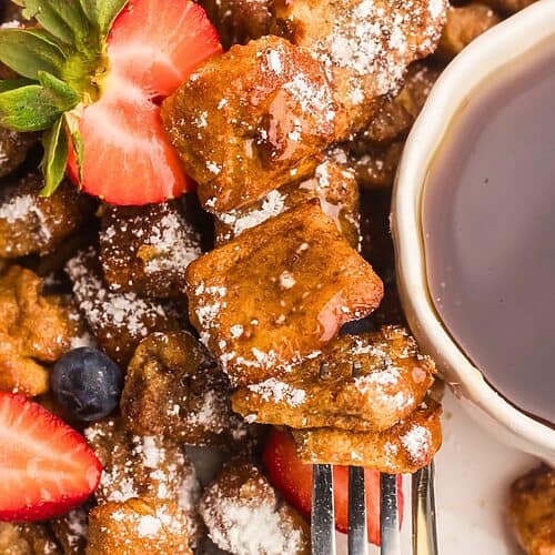 Golden French toast bites on a white plate with berries and syrup.