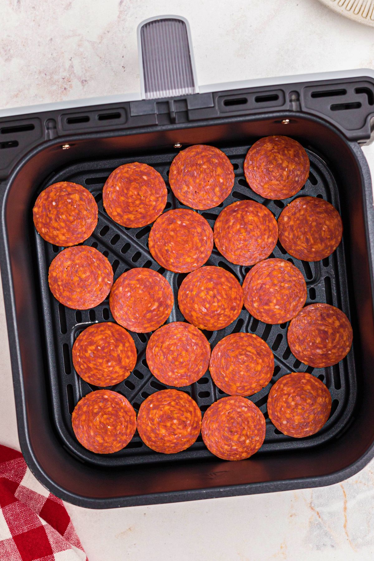 Uncooked pepperoni slices in the air fryer basket. 