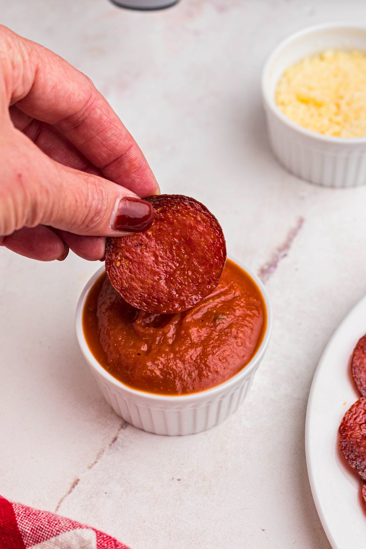 A hand dipping a pepperoni chip into a small bowl of pizza sauce. 