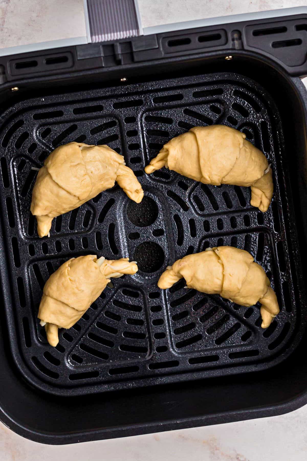 Filled crescent roll dough in the center of the air fryer basket before being cooked. 