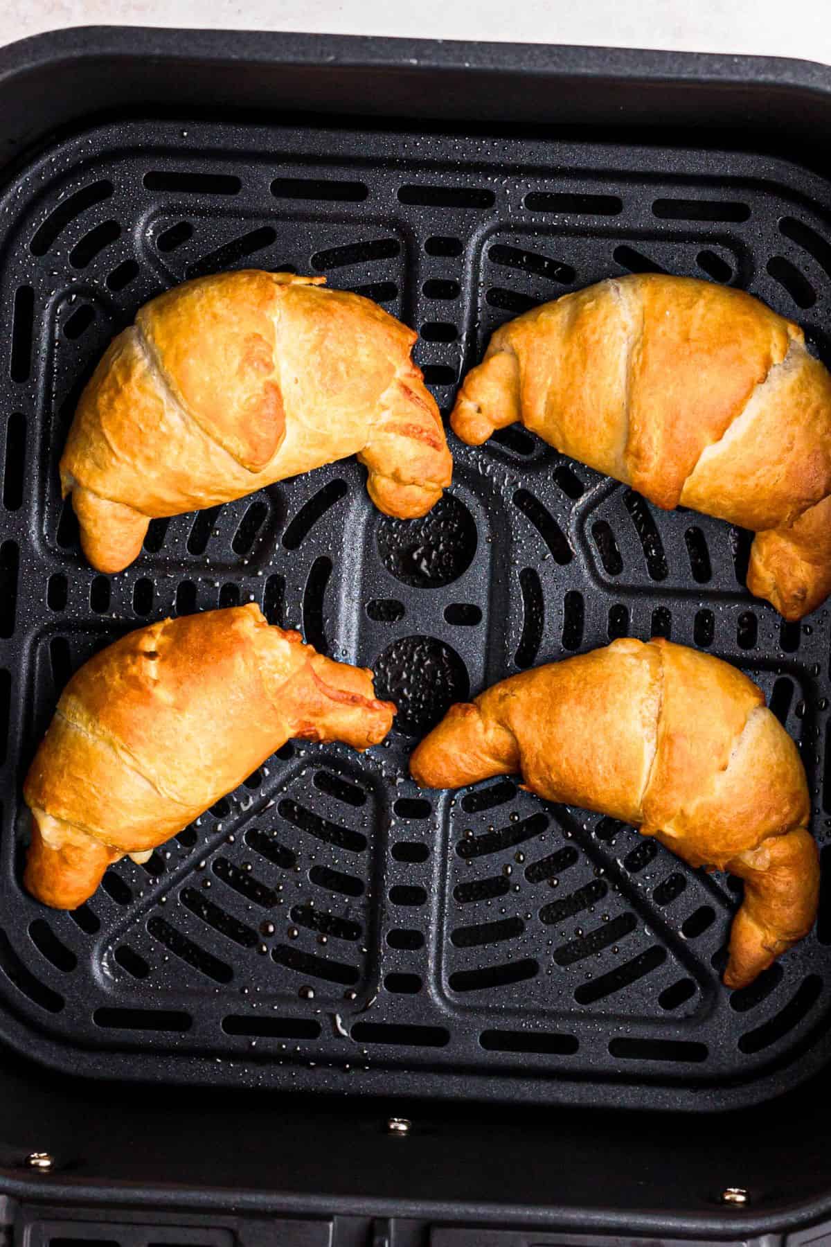 Golden crescent rolls filled with pizza toppings, in the air fryer basket after being cooked. 