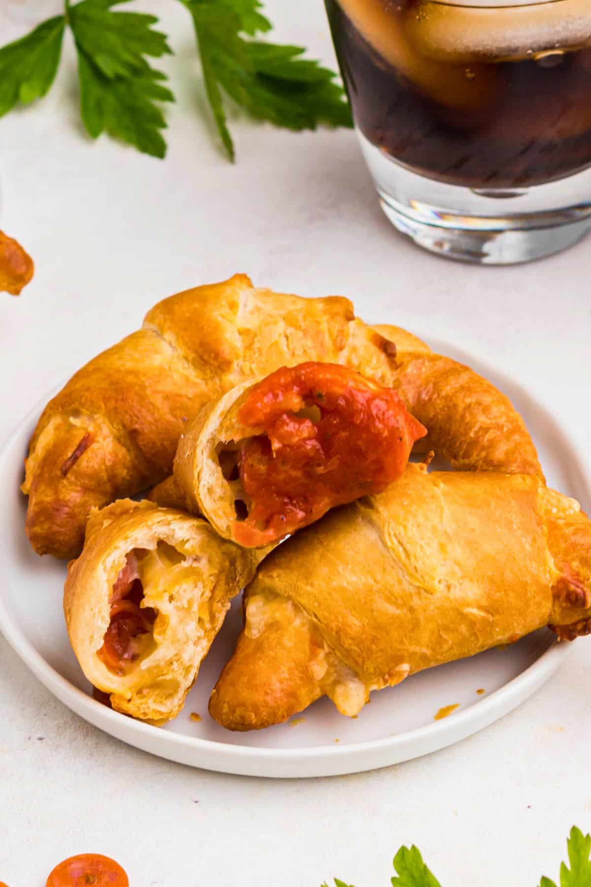 Pizza crescent rolls on a small white plate with one split open and dipped into pizza sauce. 