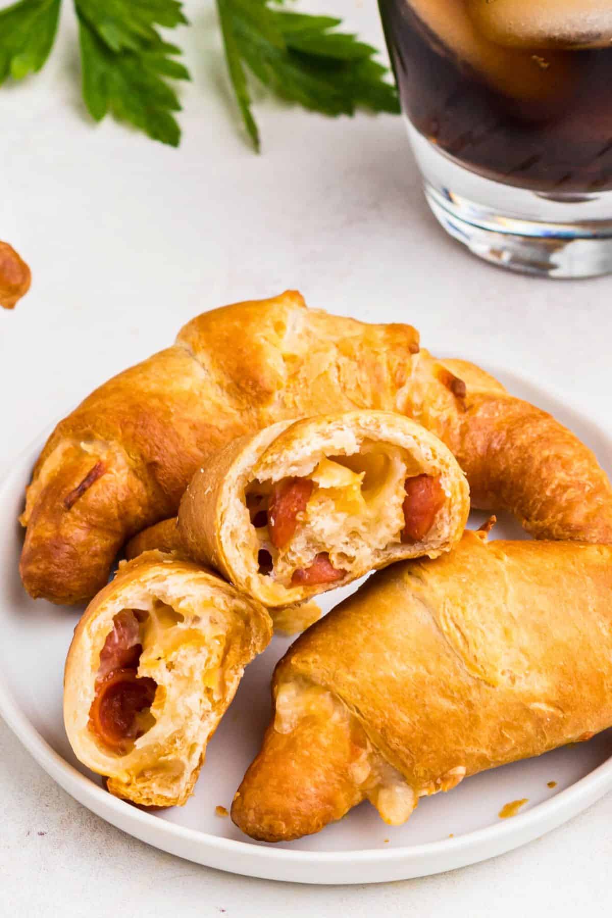 Golden pizza crescent rolls on a small white plate with melted cheese and small pepperoni . 