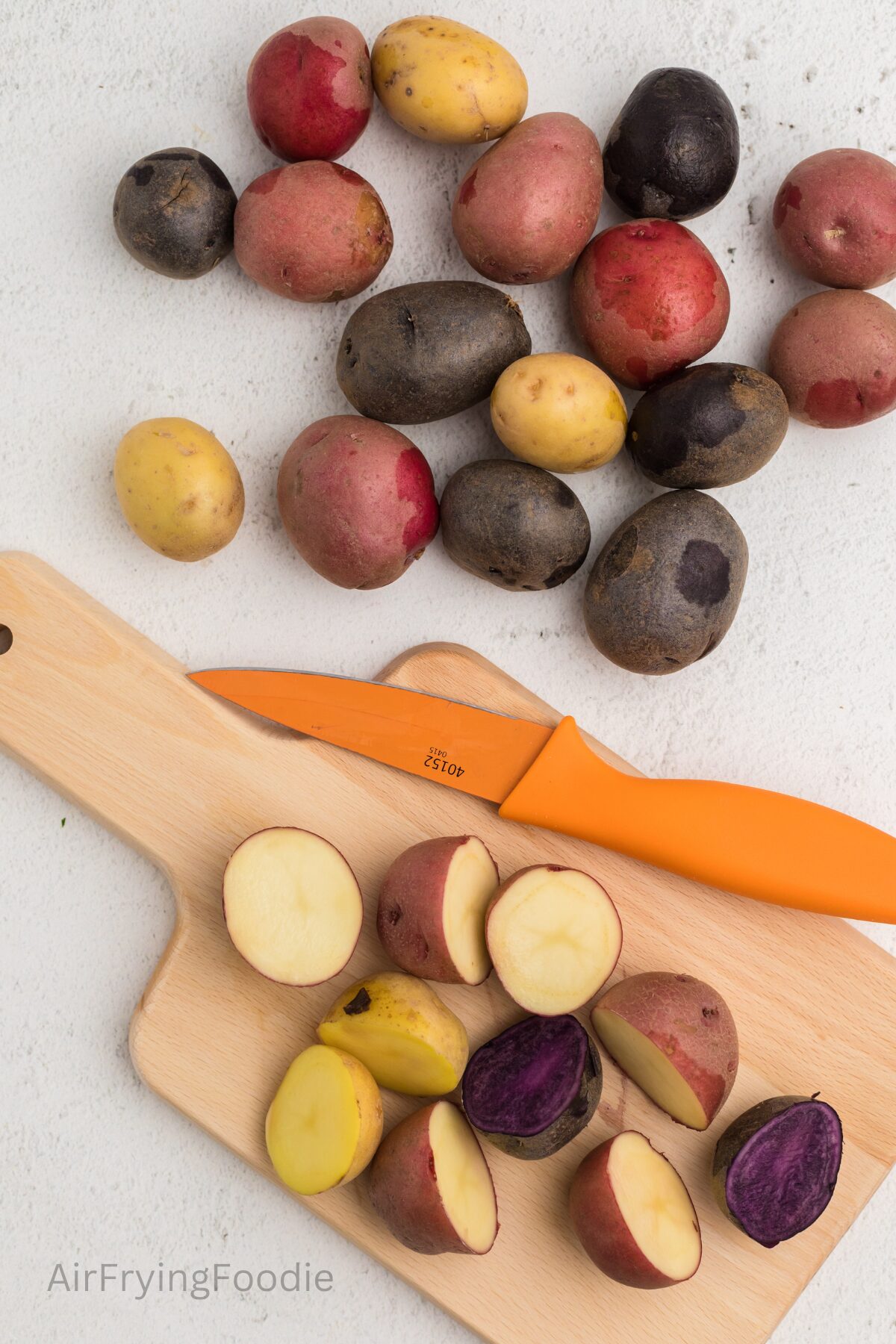 Washed and rinsed potatoes, with potatoes being cut in half on a cutting board. 