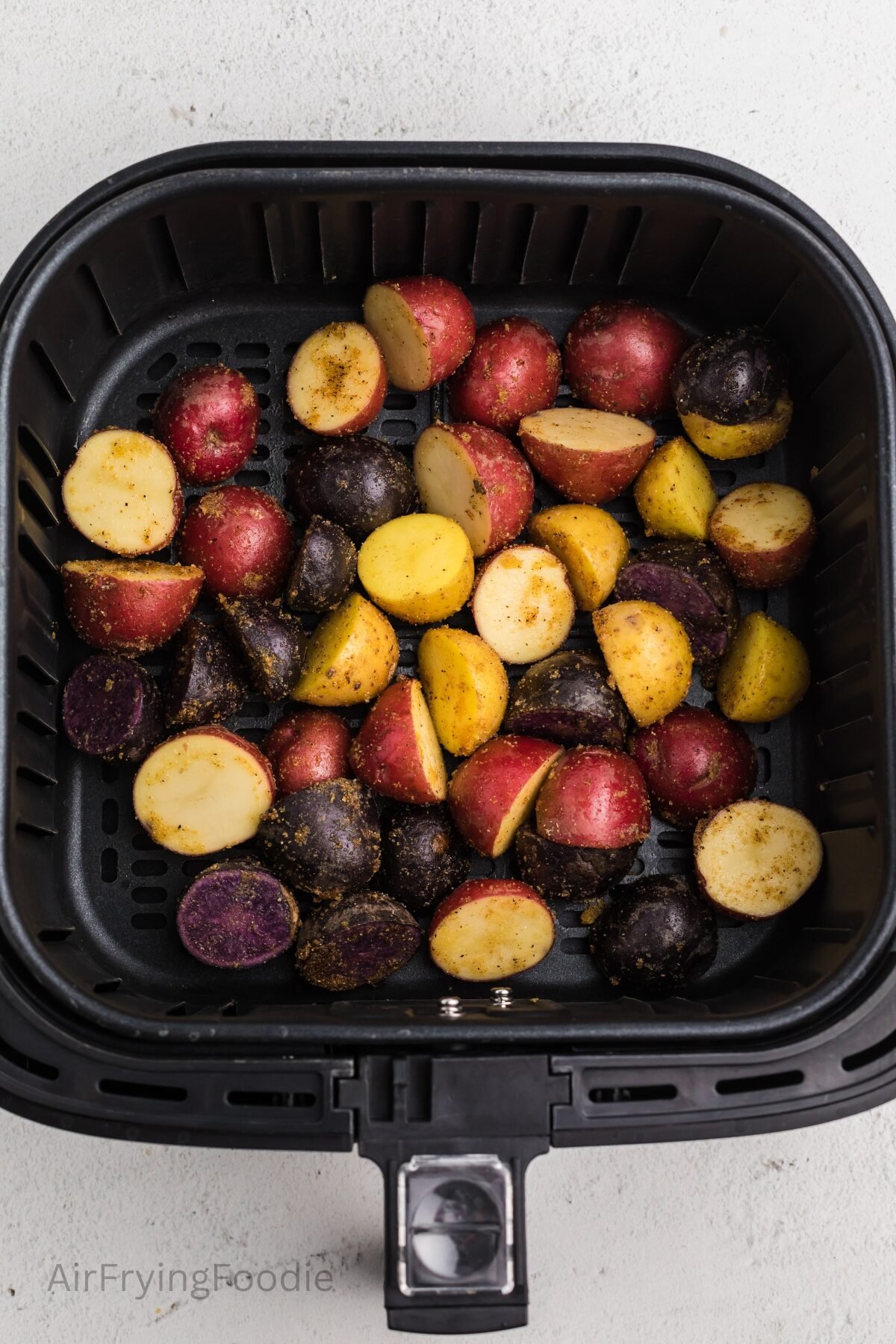 Seasoned potatoes in the basket of the air fryer, ready to be cooked. 