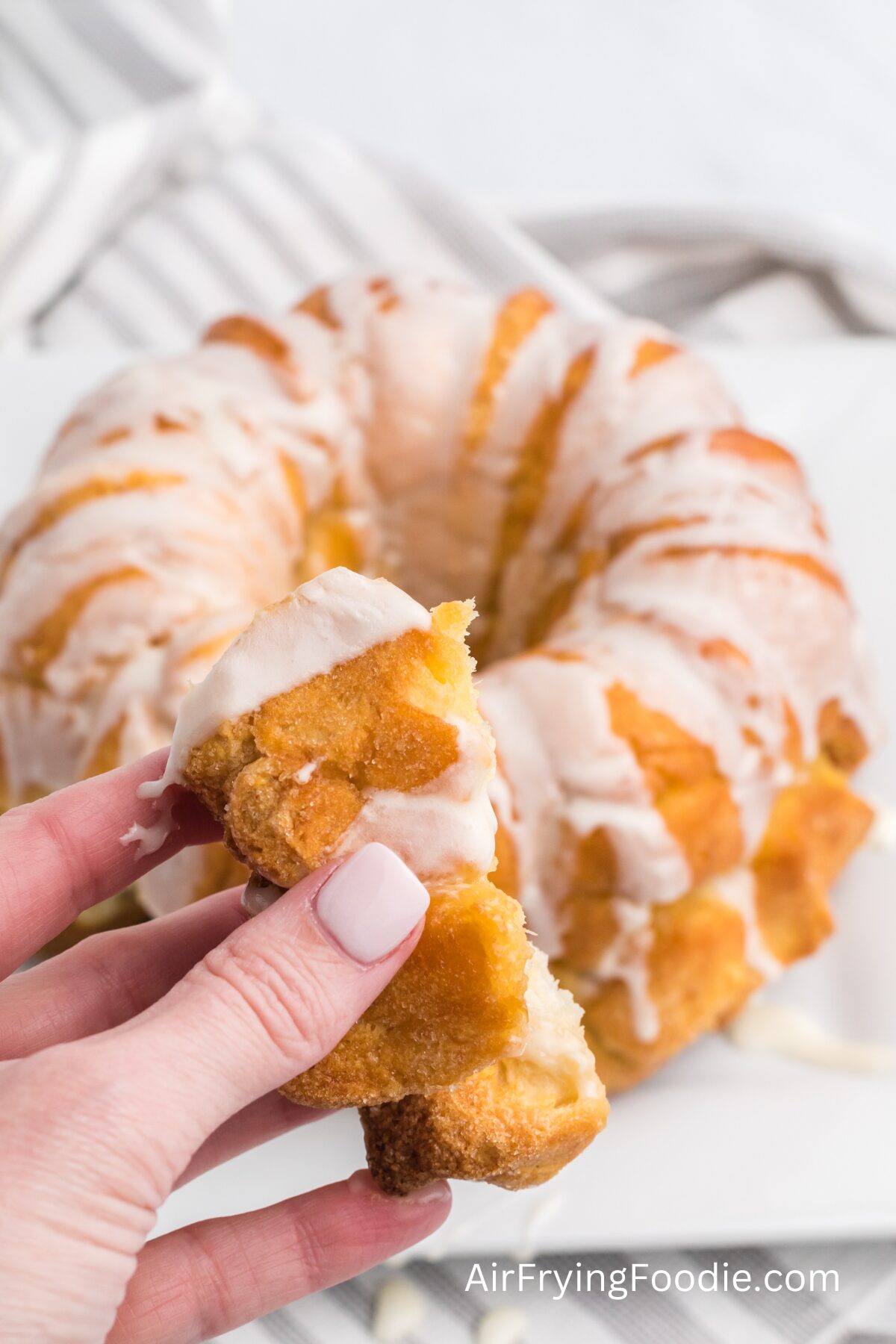 hand holding a piece of air fried monkey bread, with the monkey bread in the background. 