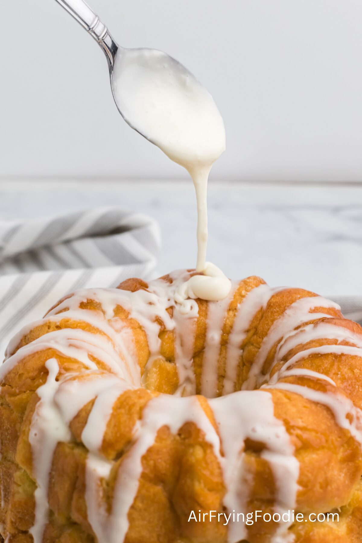 Air fried monkey bread with a spoon drizzling a sugar glaze on top before serving. 