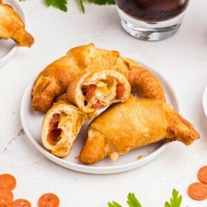 Pizza crescent rolls stacked on a small white plate with cheese and pepperoni inside.