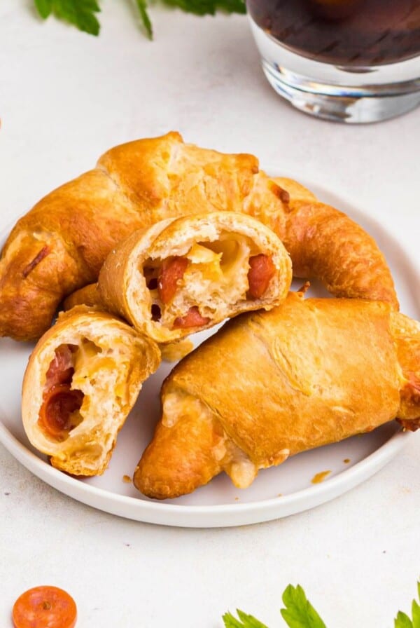 Pizza crescent rolls stacked on a small white plate with cheese and pepperoni inside.