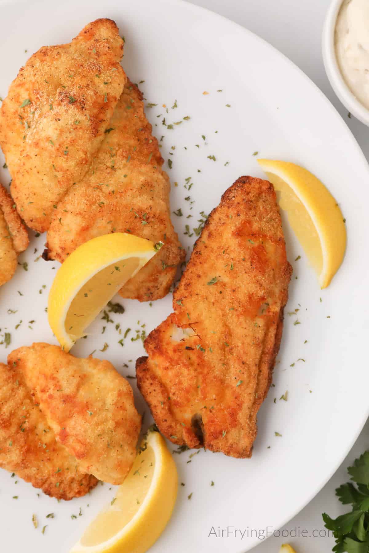 Air fried Catfish filets on a white plate with lemon wedges, ready to serve. 