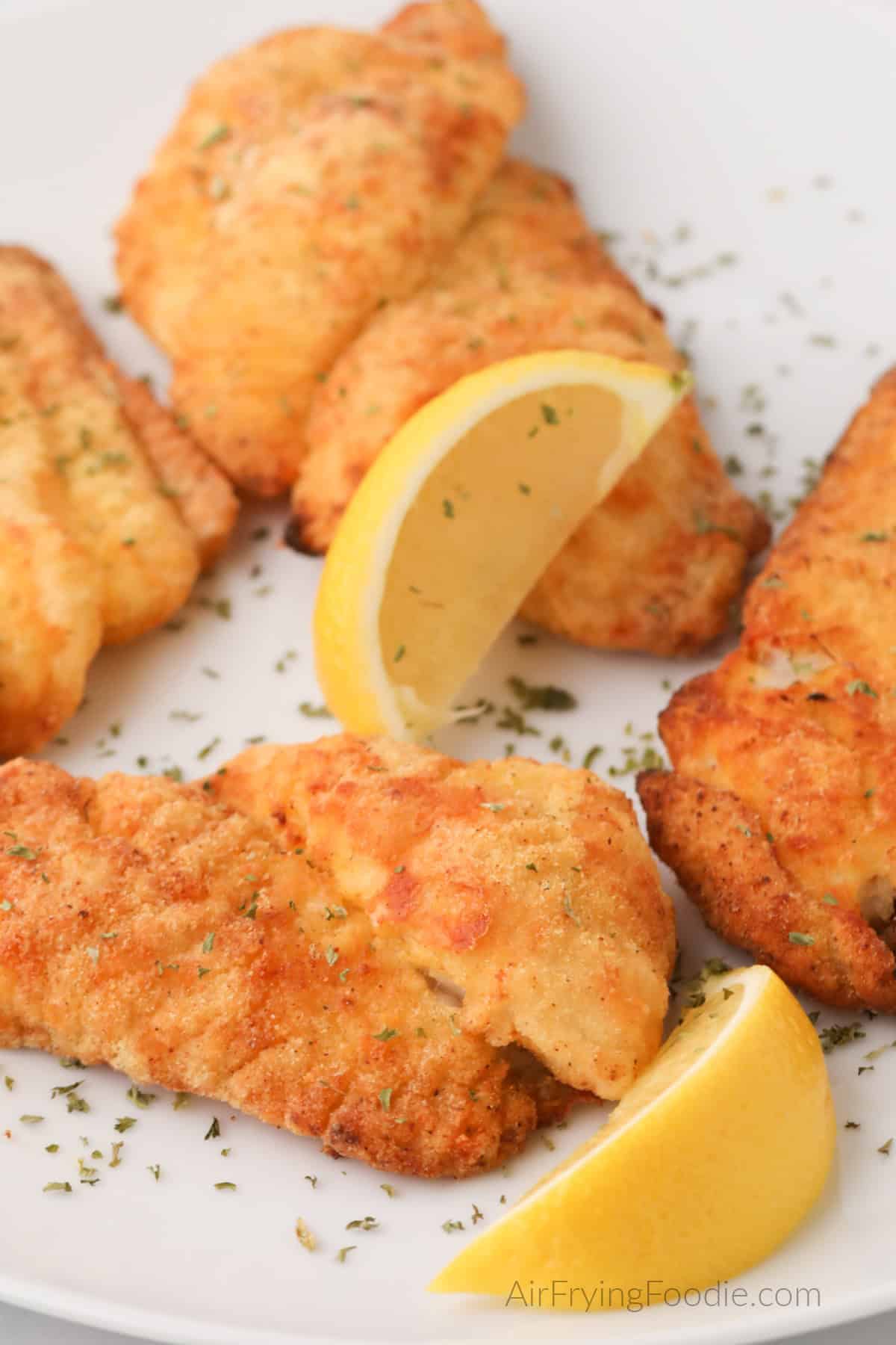 Air fried catfish filets on a white plate with lemon slices, ready to serve. 