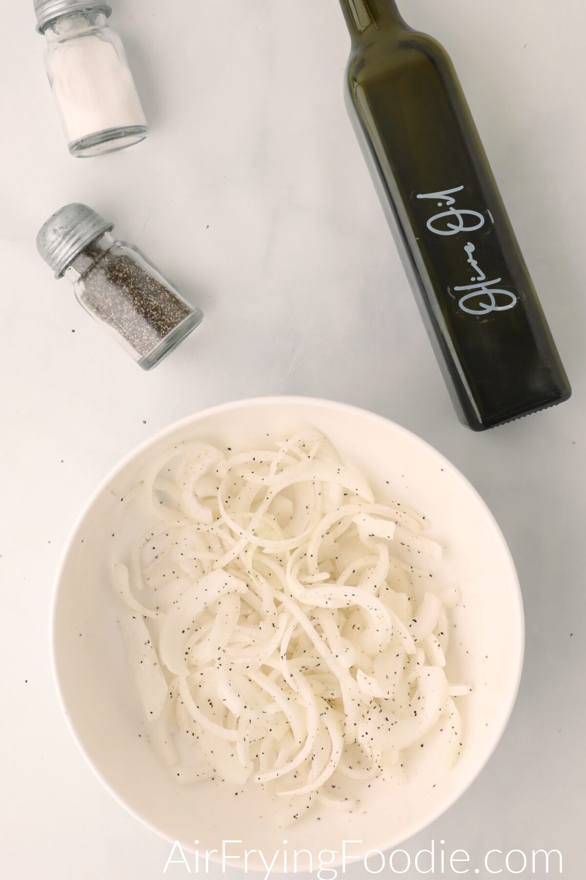 Onions sliced, in a bowl, and topped with salt, pepper, and olive oil. 