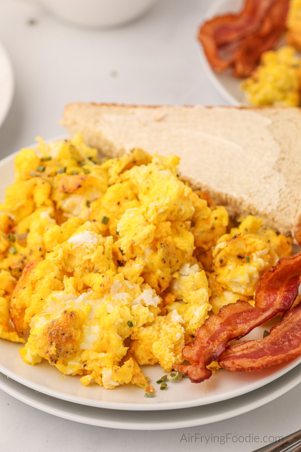 Fluffy air fryer scrambled eggs on a plate with bacon and a side of buttered bread. 