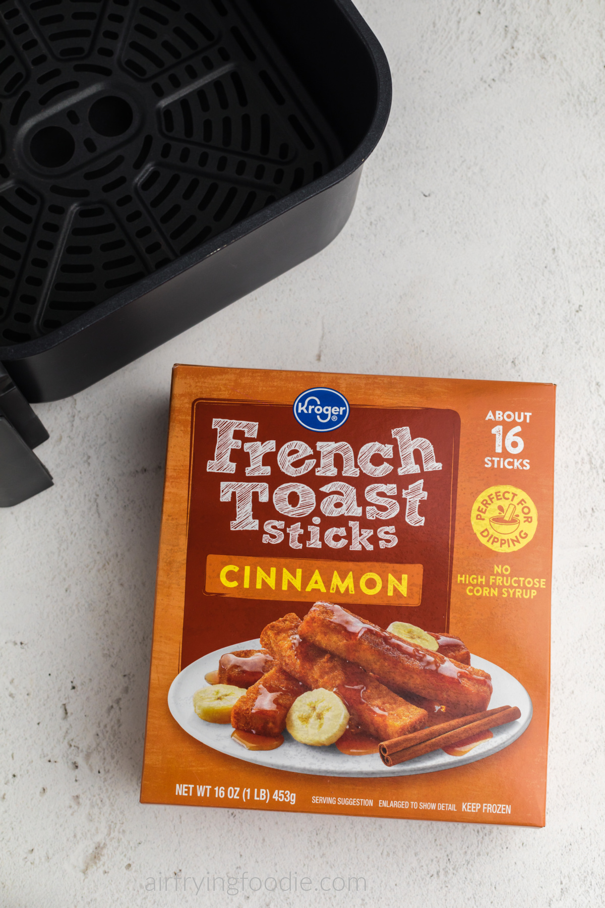 Overhead photo of frozen french toast sticks in a box and a basket of an air fryer. 