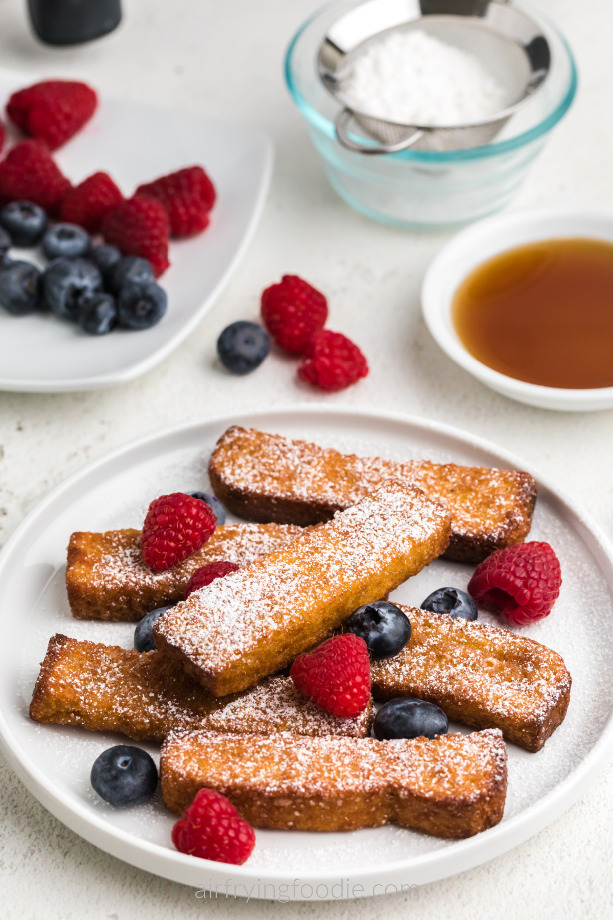 Air fryer frozen french toast sticks fully cooked and served on a white plate with berries and powdered sugar. Ready to eat. 