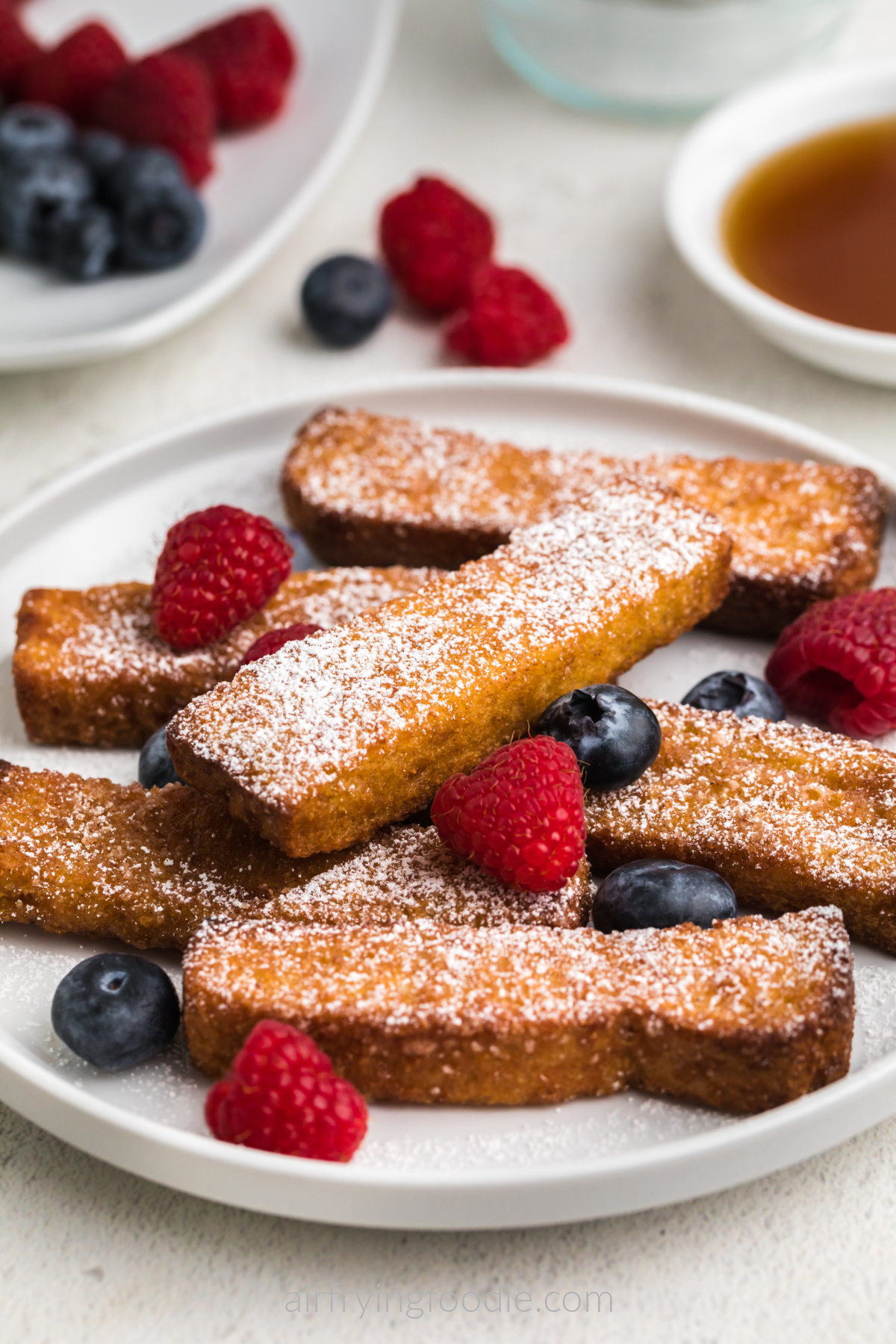 Close up photo of air fryer frozen french toast sticks on a white plate with powdered sugar and berries. 