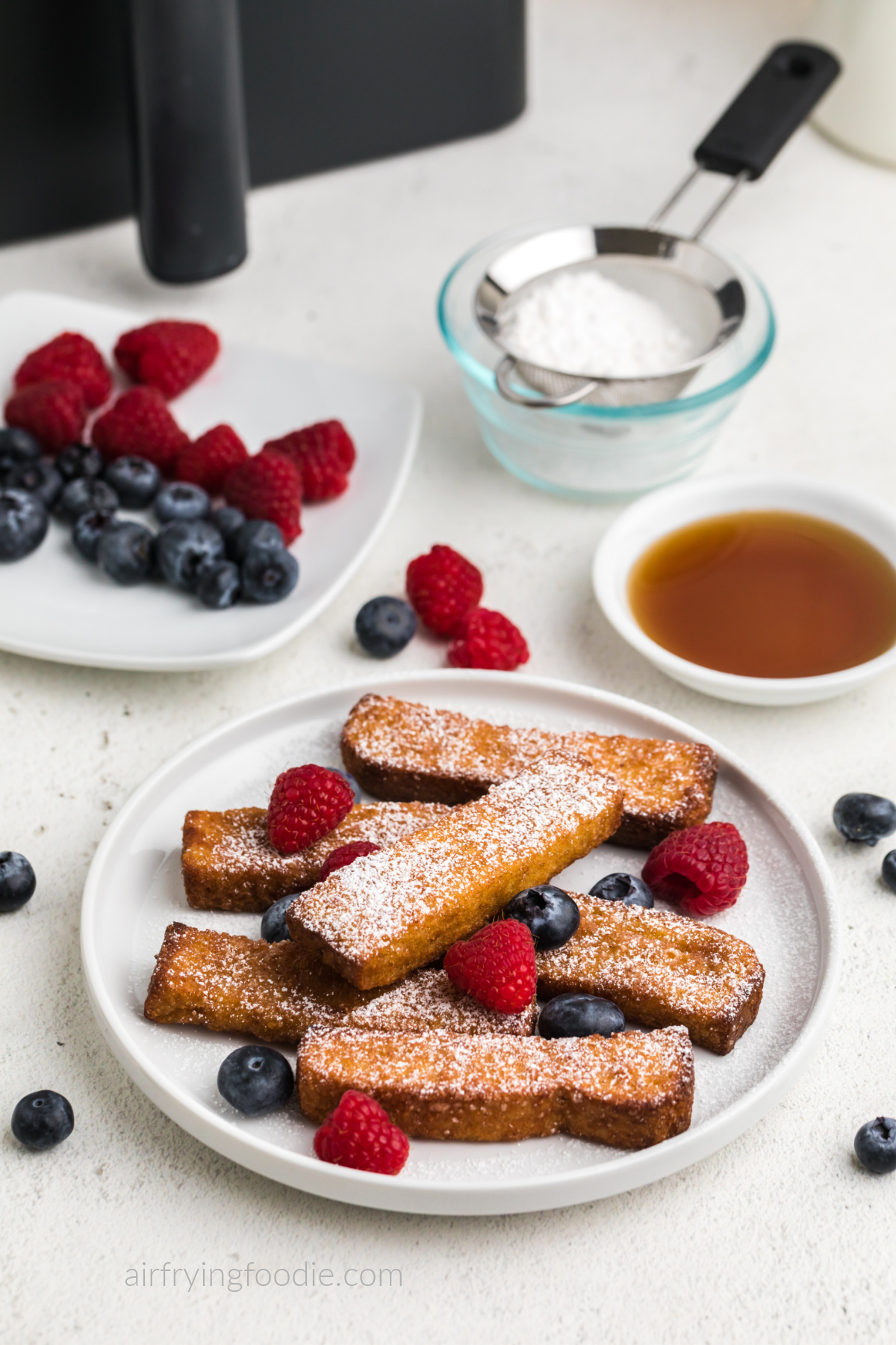 Air fryer frozen french toast sticks on a white plate with berries and powdered sugar. Ready to eat. 