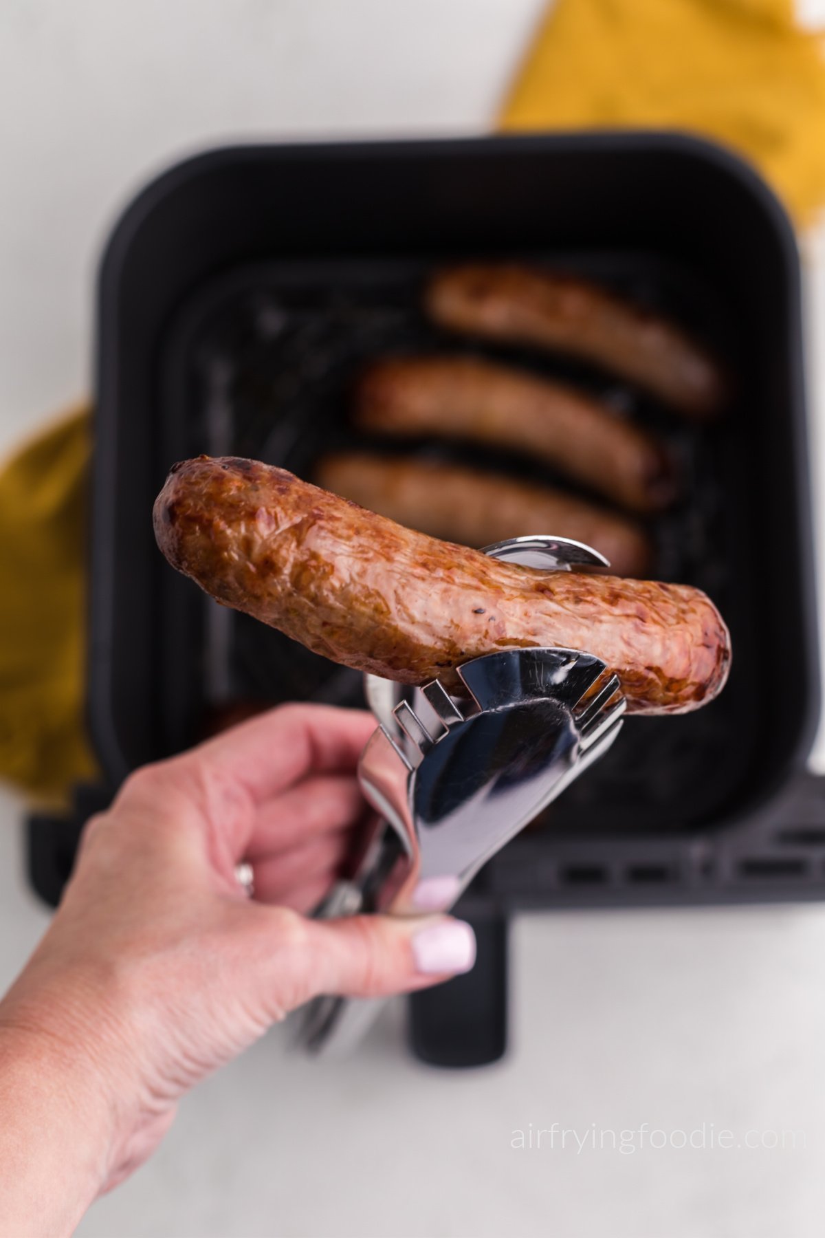 Juicy air fried Italian sausage in tongs, ready to serve. 