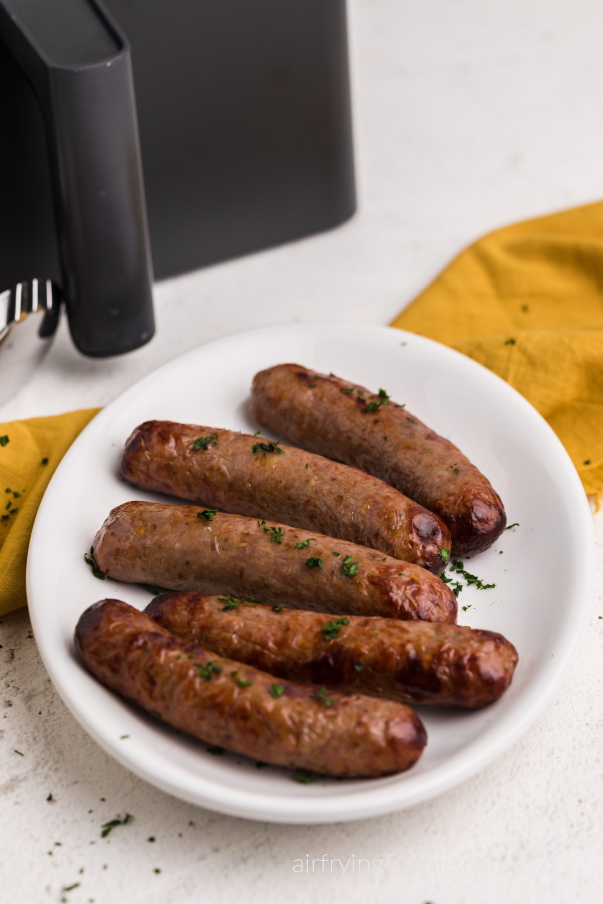 Italian sausages made in the air fryer, served on a white platter with parsely garnish on top. 