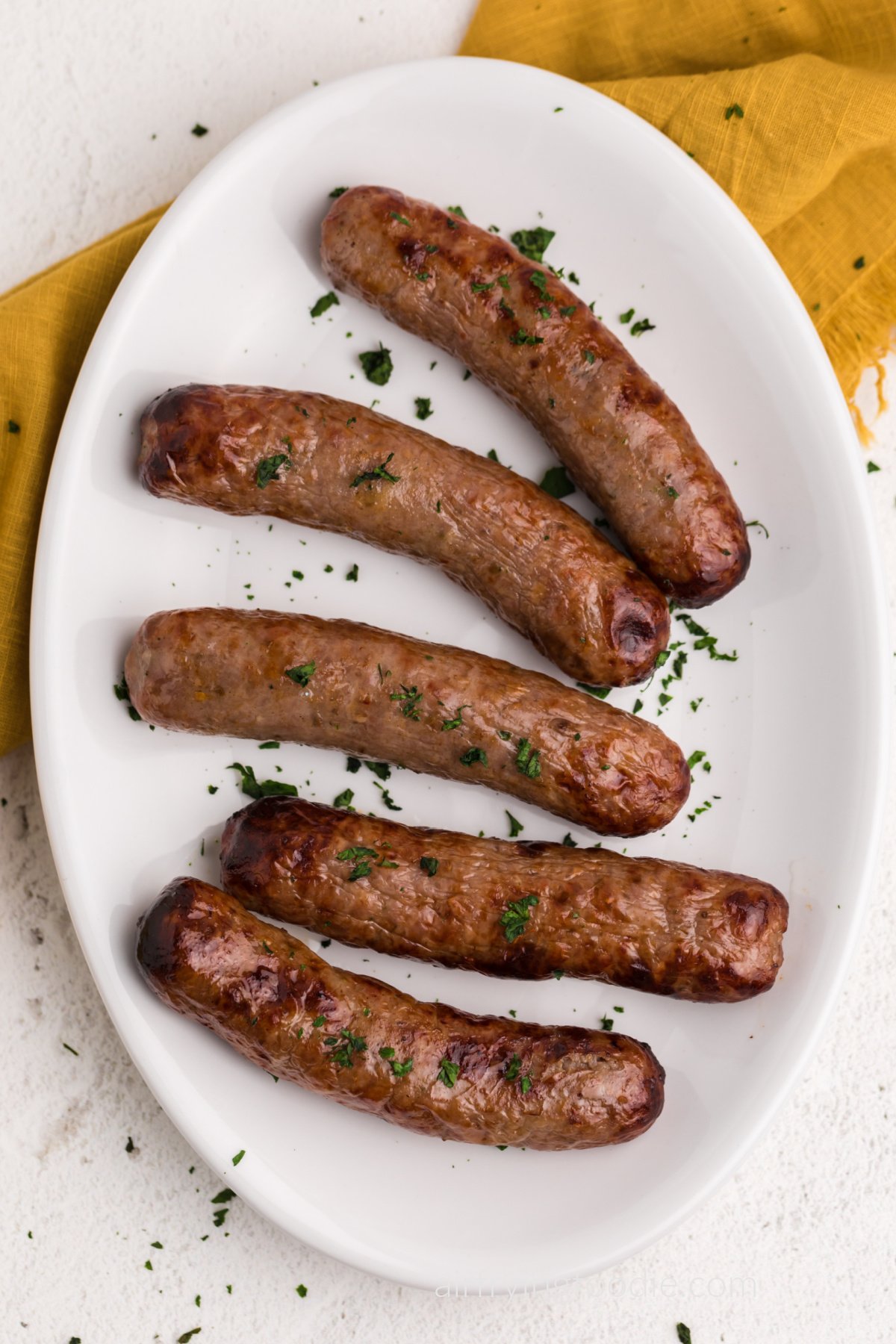 Close up of air fryer Italian sausage on a white serving platter garnished with parsley. Ready to serve. 