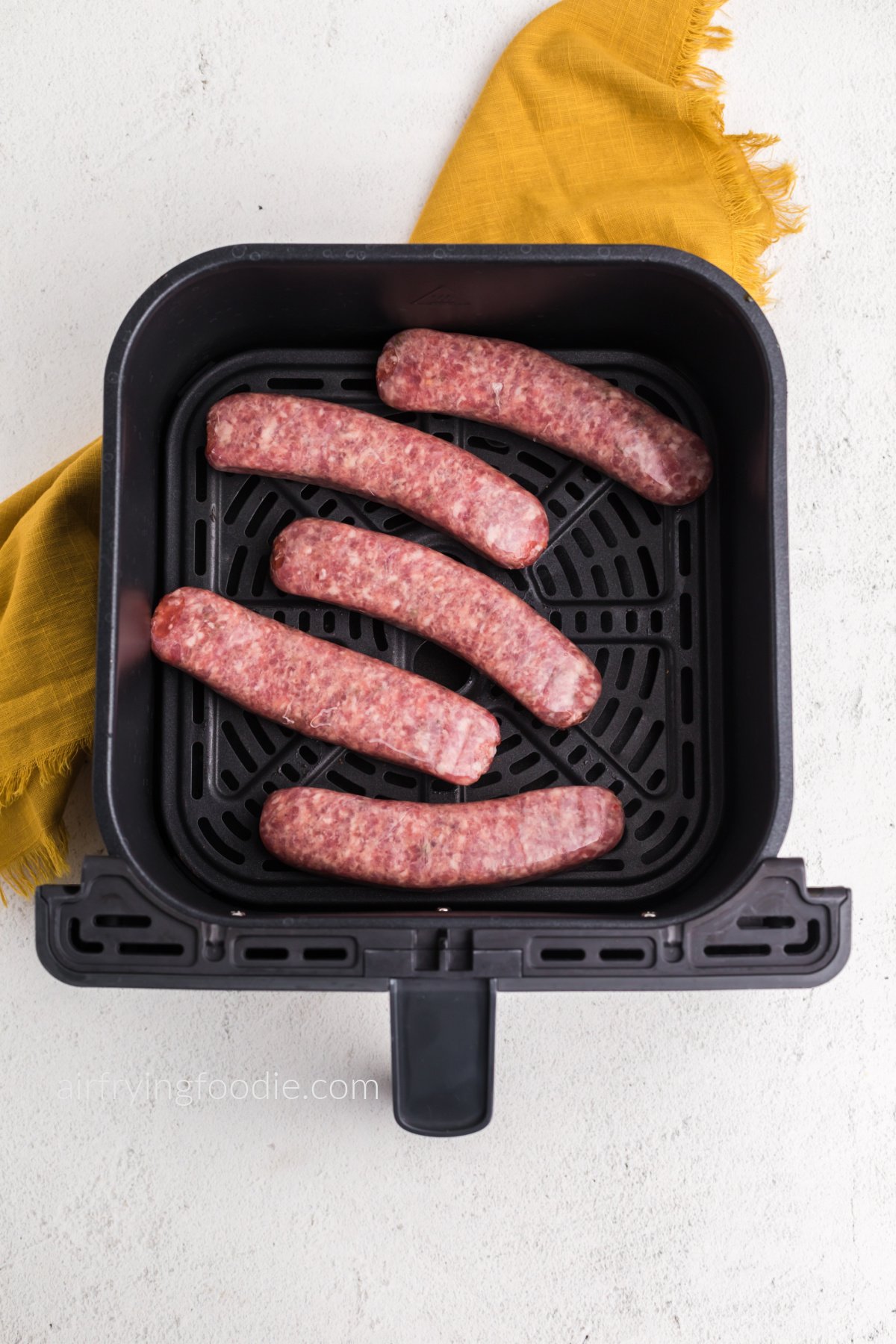 Italian sausage in air fryer basket in a single layer, ready to be cooked.