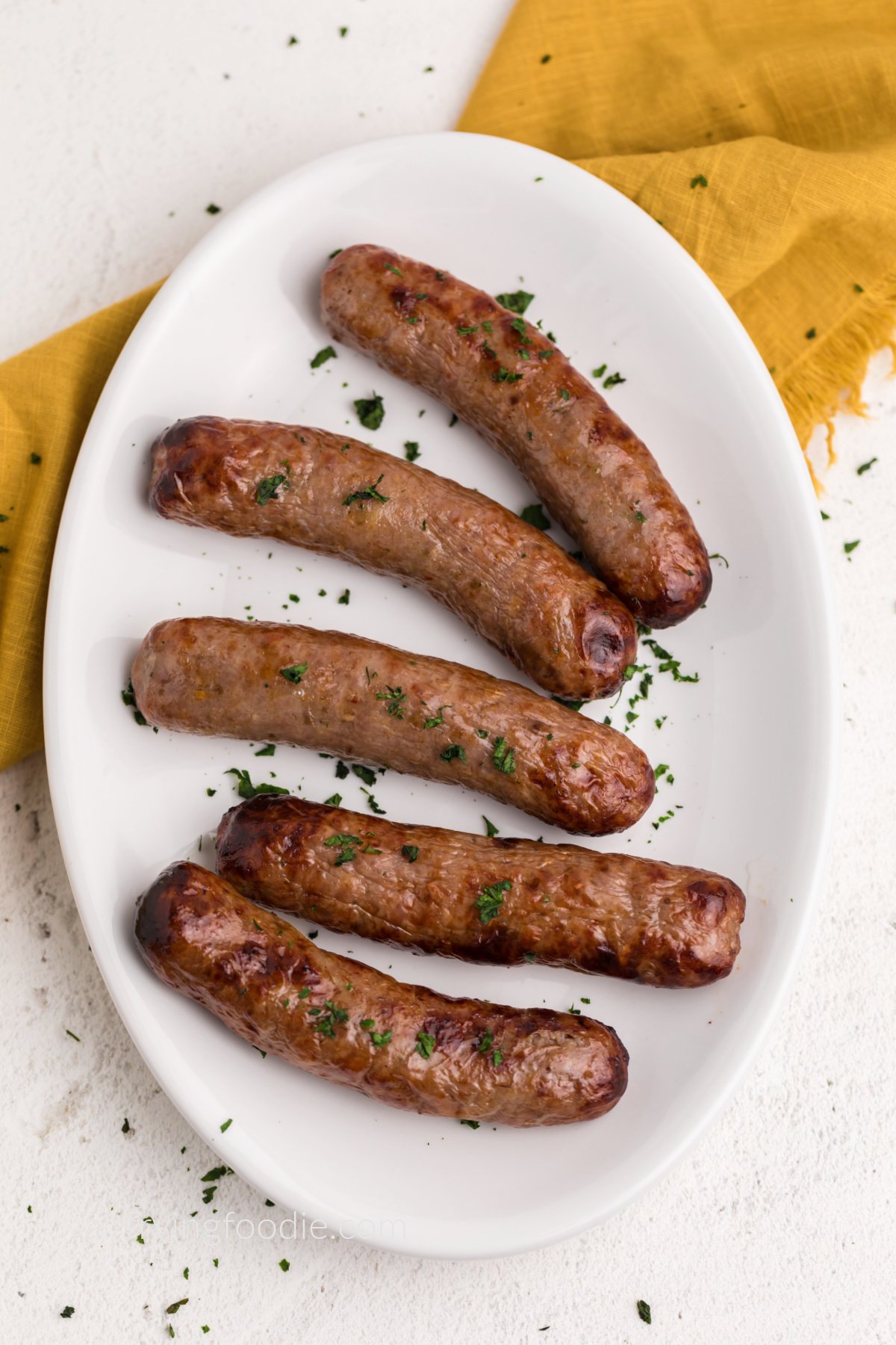 Air fried Italian sausage on a white plate garnished with parsley flakes, ready to serve. 