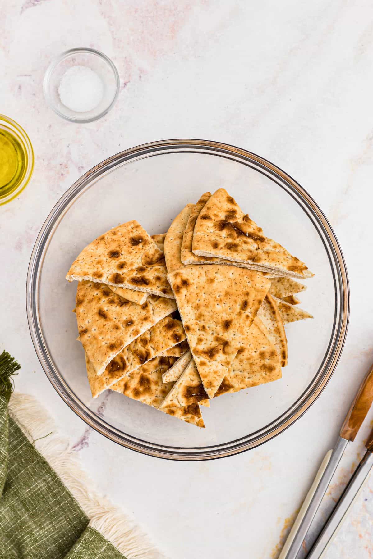 Pita bread cut into triangles, tossed with olive oil and salt in a clear glass bowl. 